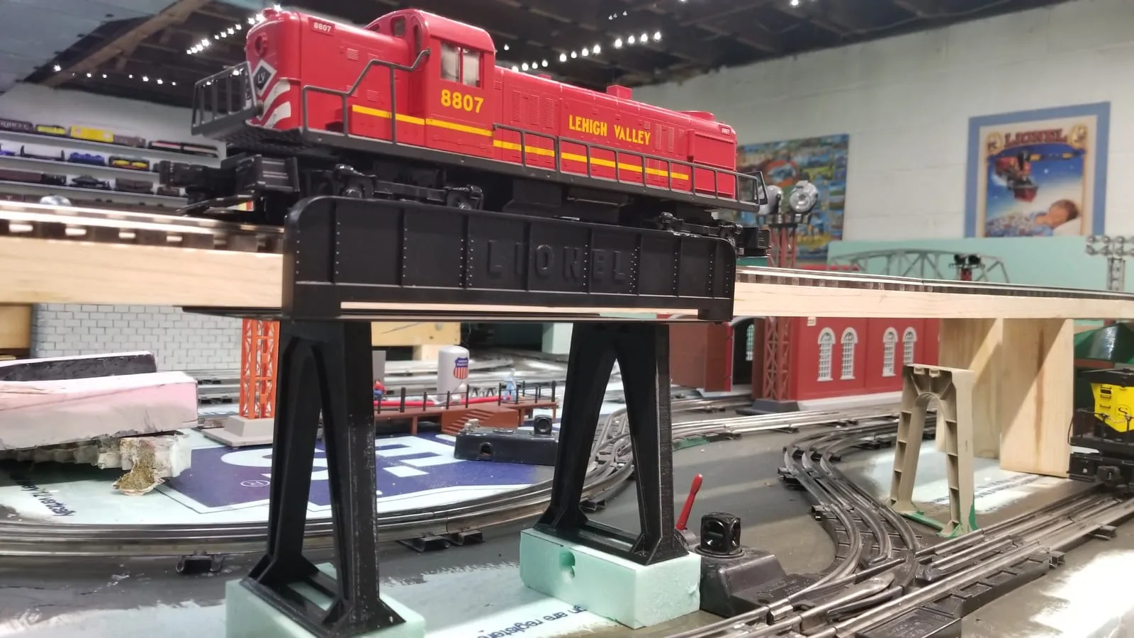 A black 3D-printed truss bridge carrying a red O-scale locomotive on a model railroad layout.
